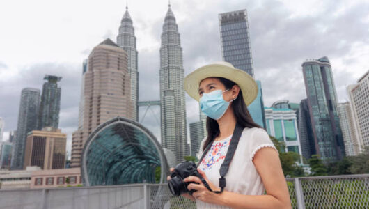 Female tourist wearing protective face mask and taking photos with camera in Kuala Lumpur, with  cityscape as background